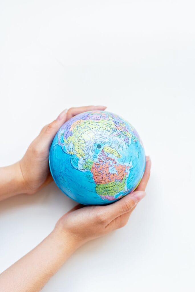 A close-up of hands gently holding a colorful globe against a white background.